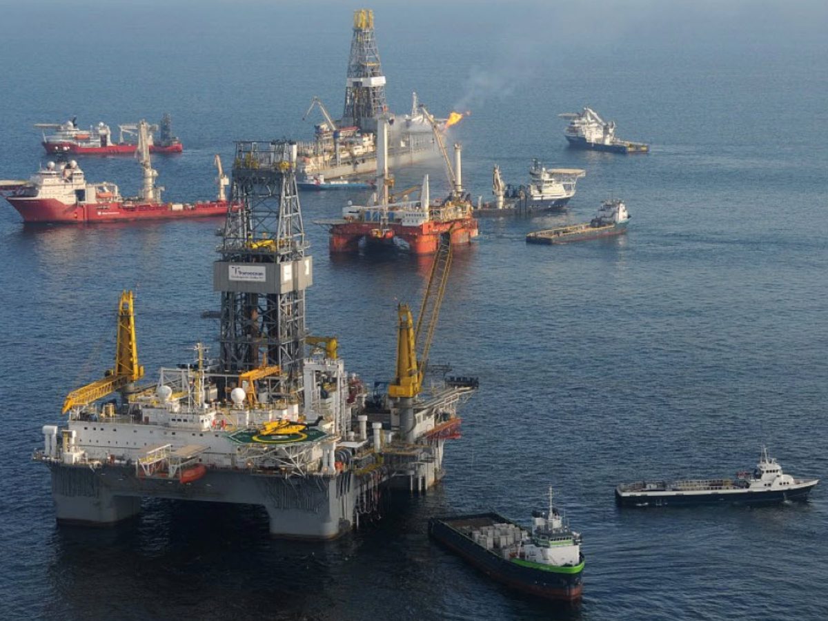 A group of boats in the ocean with oil rigs.