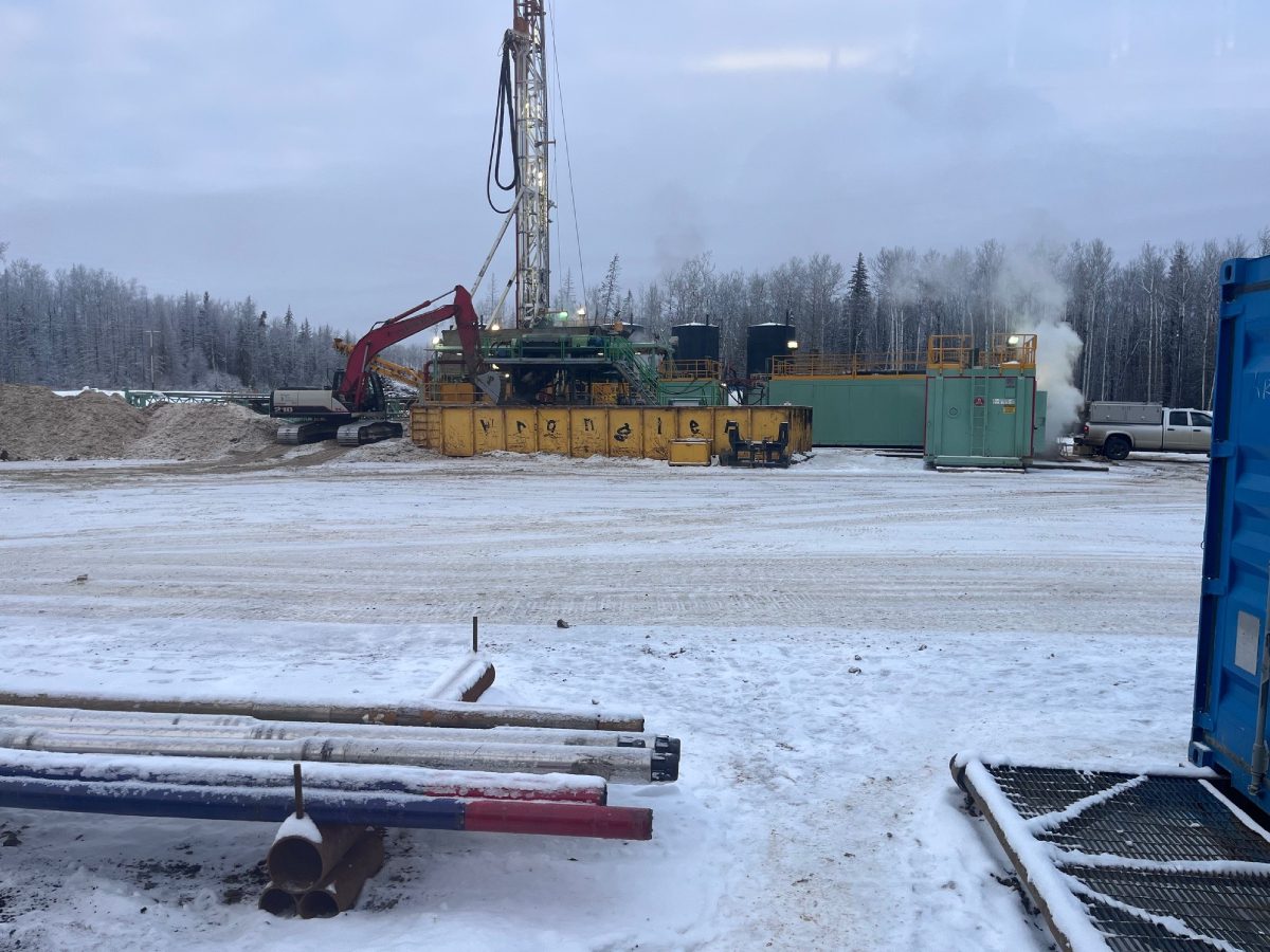 A drilling rig in the snow with pipes and poles.